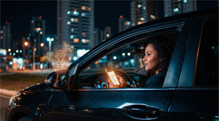 Mulher no carro à noite usando app de rastreamento veicular para segurança com ícone GPS laranja em Goiânia